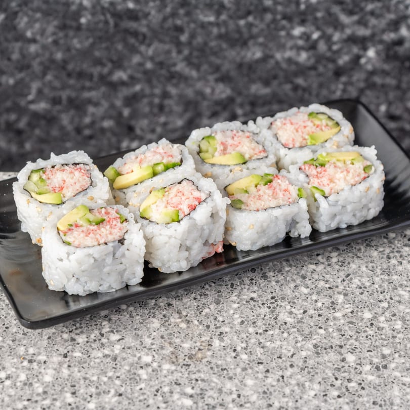 Eight California sushi rolls with crab, avocado, and rice, served on a black plate.